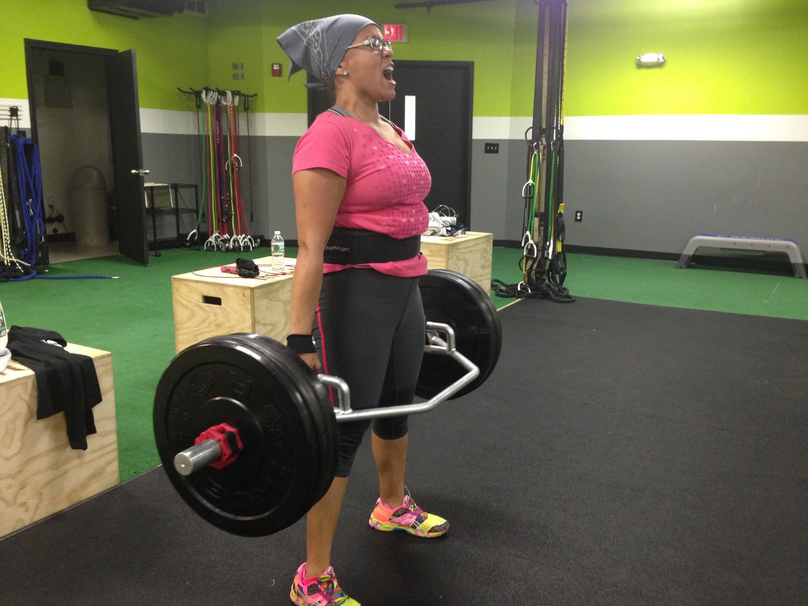 A member of The F.I.T.T. PIT mid-deadlift, trap bar loaded, green wall behind her